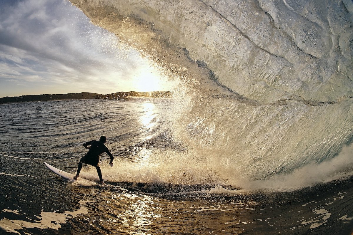 A surfer with a ocean wave above him taken by one of the best sports photographers Russell Ord
