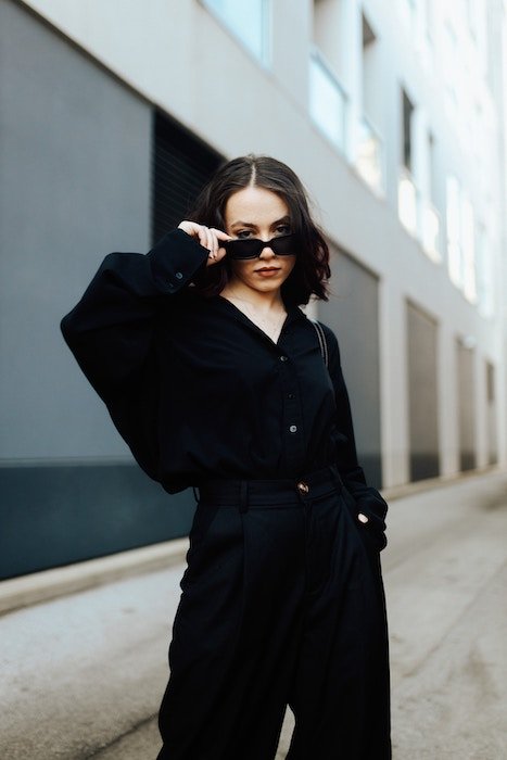 A woman in black clothing posing for a portrait by lowering her sunglasses