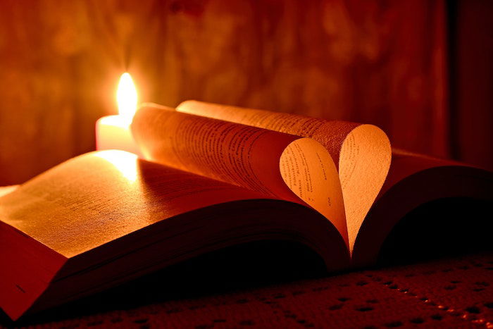 A book with pages folded in the shape of a heart backlit by a lit candle