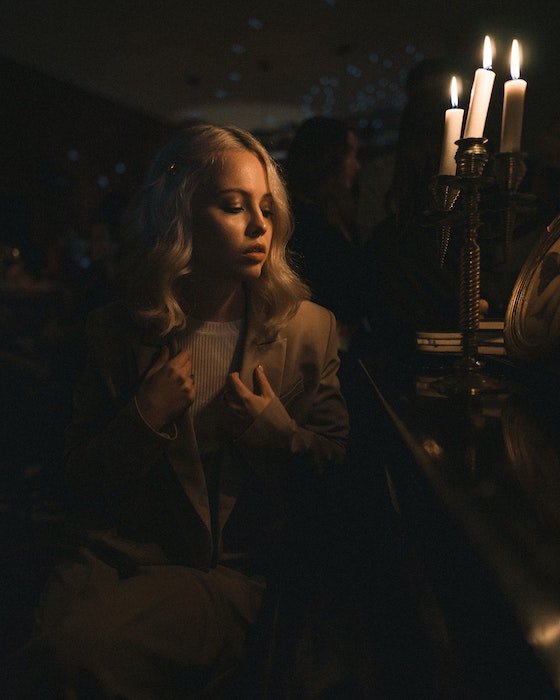 A dim light portrait of a woman wit her eyes closed posing by three lit candles in a candelabra