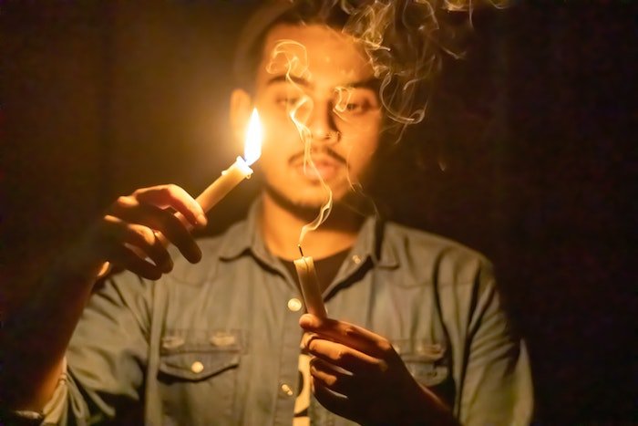 A person holding a lit candle above another smoking candle as an example for creative lighting ideas