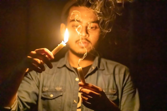 A candlelight photo of a person holding one lit candle and one candle with smoke trailing off the wick