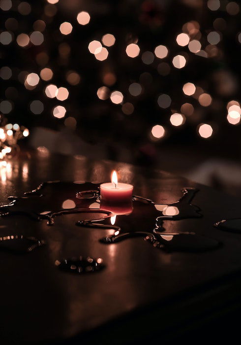 A lit tea light on a table of melted wax with soft bokeh in the background