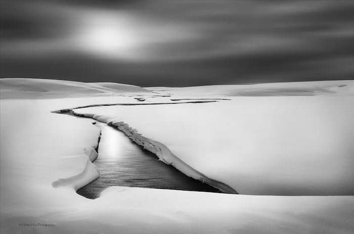 black and white landscape photography: a slow river flowing through untouched snow