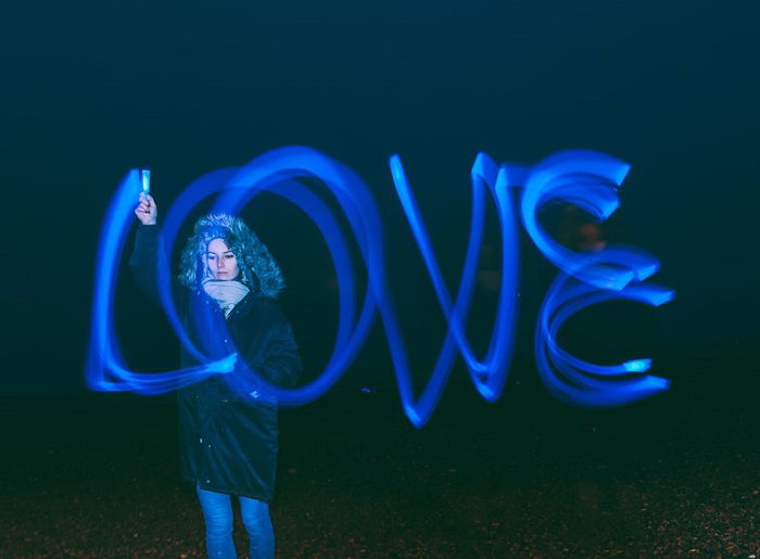 A person is holding a blue light pen that is creating the word love with their hand. 