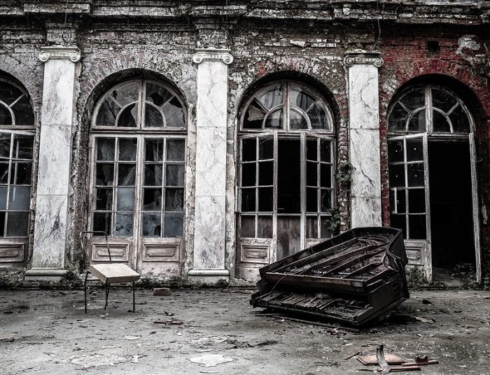 a destroyed grand piano in front of broken arched windows 