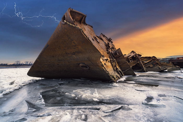 Rusted shipwreck on icy water with lightning in the sky