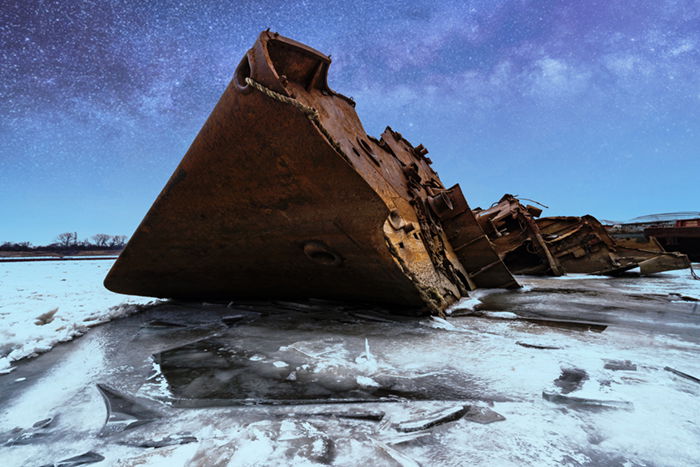 Rusted shipwreck on icy water with a starry sky added using Picnic