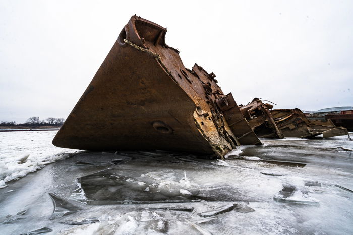 Rusted shipwreck on icy water with cloudy washed out sky