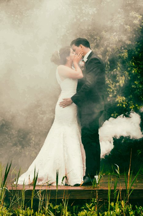 a wedding photo of a couple kissing by a lake surrounded by smoke