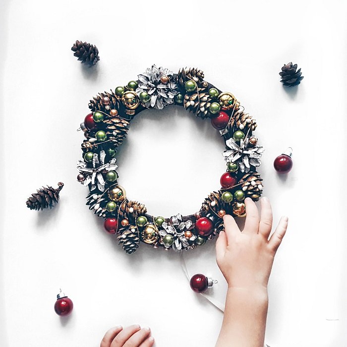 Christmas flat lay of a child's hand touching a pine cone wreath