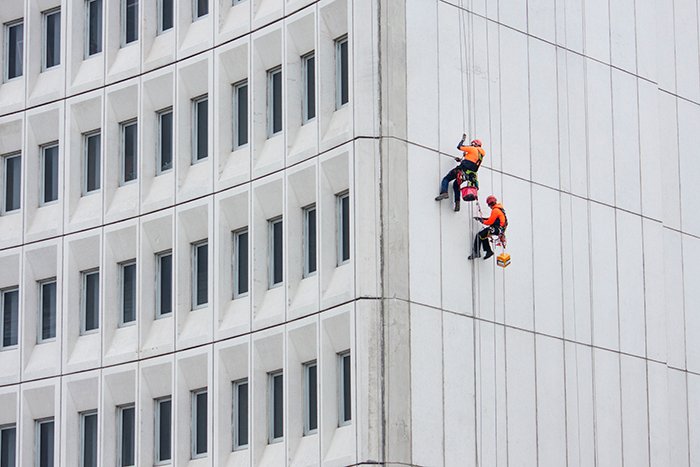 two workers dressed in bright orange suspended from the side of a white building showing a pop of color in photography