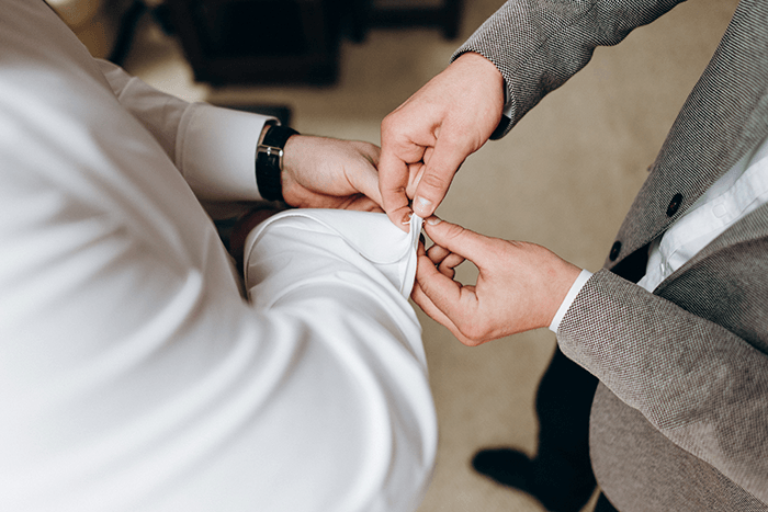 groomsmen photography: a photo of a groomsman helping put cufflinks on the groom
