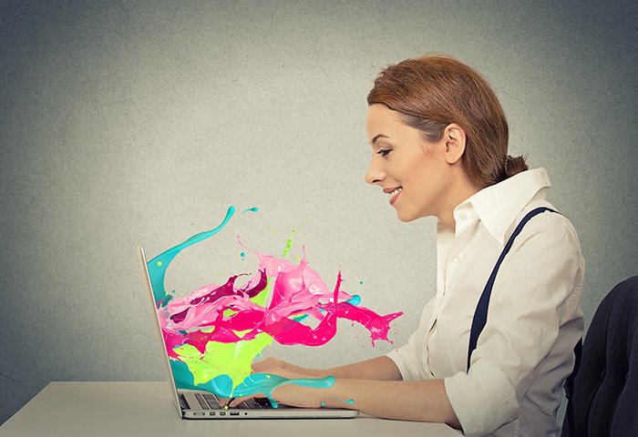 Side view profile attractive happy young business woman working on laptop computer colorful splashes coming out of screen liquid effect isolated grey wall background. Positive face expression vision