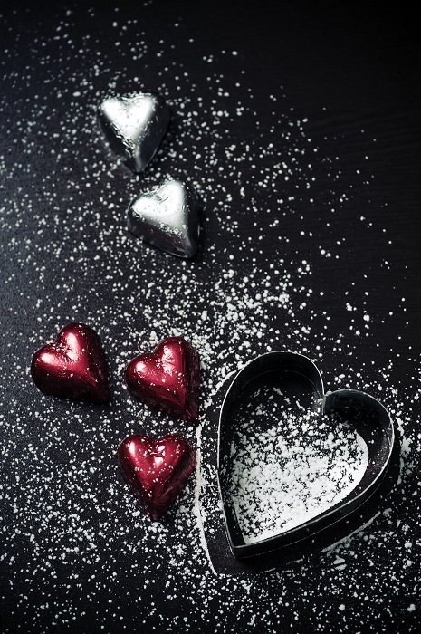 flat lay background idea: heart shaped chocolates and cookie cutter sprinkled with confectionary sugar on a black background
