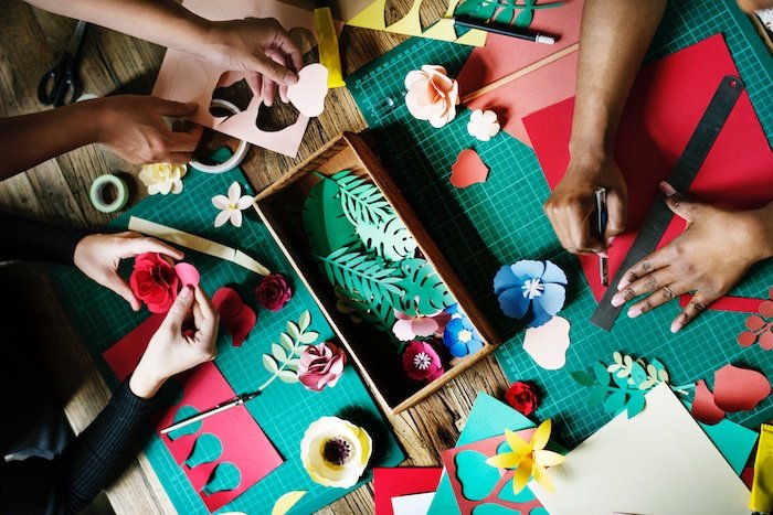 flat lay photo idea: Image from overhead of people's hands and arms glueing, cutting, and drawing on colored paper