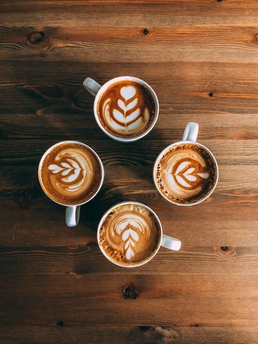 flat lay photography: A tabletop shot from above of four cups of coffee with foam designs