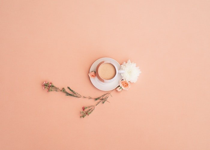 Flat lay of a cup and saucer beverage with flowers on a sparse background
