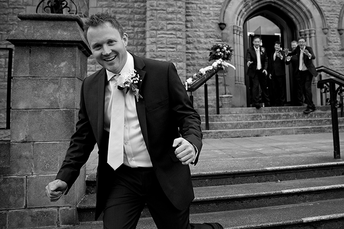 a black and white image of a groom running from the wedding