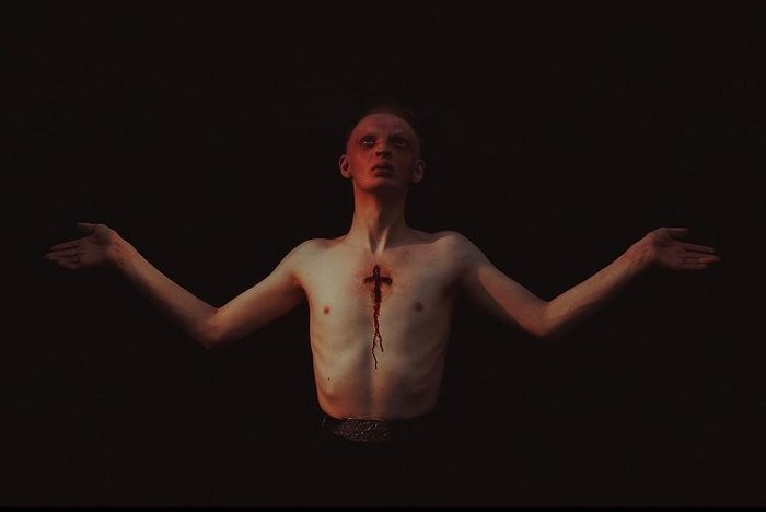 horror photography example: a man with a blood red face and a bloody crucifix engraved on his chest stretches his arms