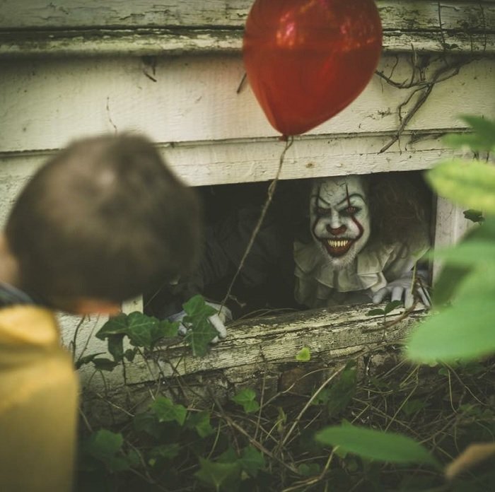 scary horror photography: Pennywise the clown peering out of a basement window at a boy 