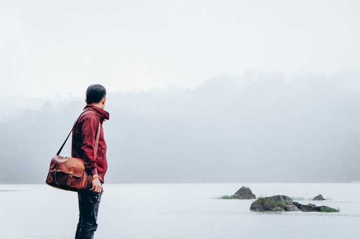 A photographer with an over the shoulder leather camera bag looking at a lake