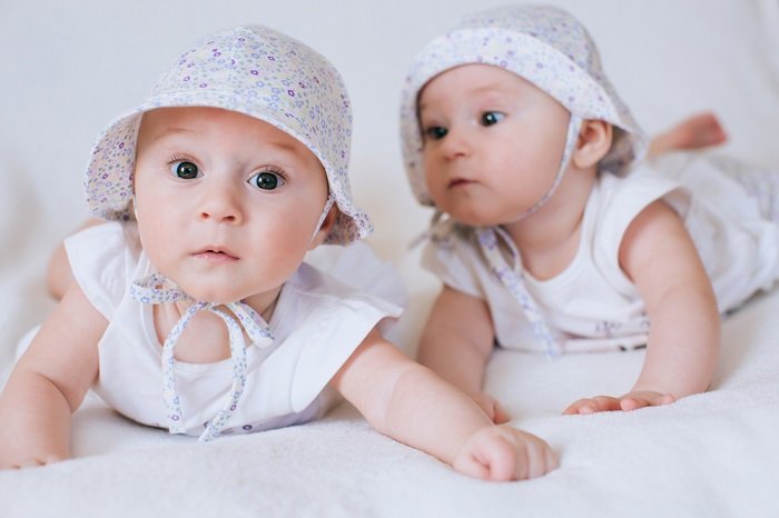 新生儿双胞胎拍摄：新生儿双胞胎，配套服装和帽子躺在他们的胃上