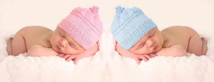 newborn twins photography: newborn twins in pink and blue knitted hats posed with their heads resting on their crossed arms