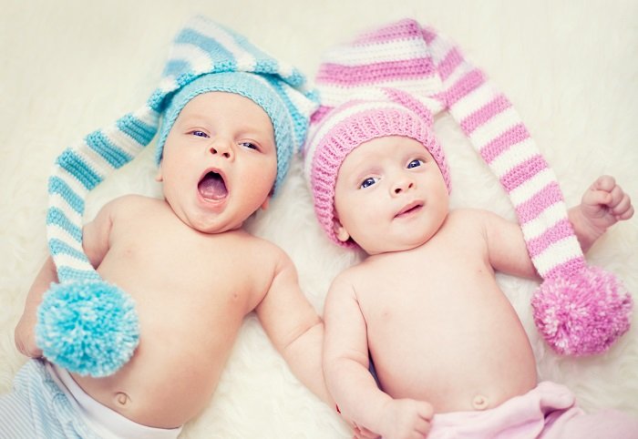 newborn twins photo ideas: one newborn twin in a blue hat yawns as the other lays next to him in a pink hat