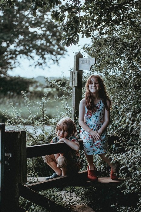 photo ideas for siblings: siblings sitting on a wooden gate in the countryside