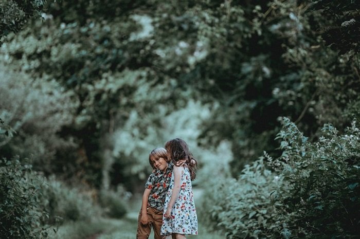 photo ideas for siblings: siblings hugging with green bushes in the background