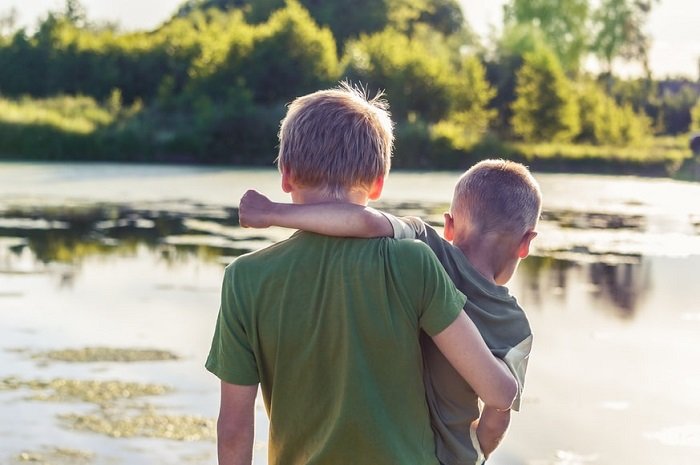 photo ideas for siblings: brothers facing over a lake on a sunny day