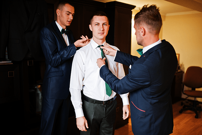 groomsmen getting ready: two groomsmen adjusting a groom's tie