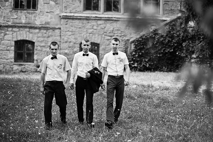a black and white photos of three groomsmen walking to the wedding