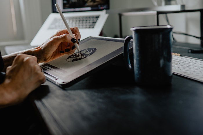 A person using a pen to edit an image on a drawing tablet on a desk with a mug and computer equipment