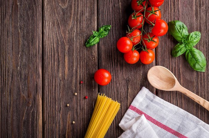 Flat lay of pasta tomatoes basil a wooden spoon and tea towel on a wood panel table