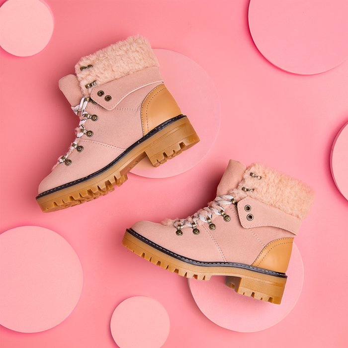 A flat lay product photography image of a pair of boots on a layered pink background with pink circles