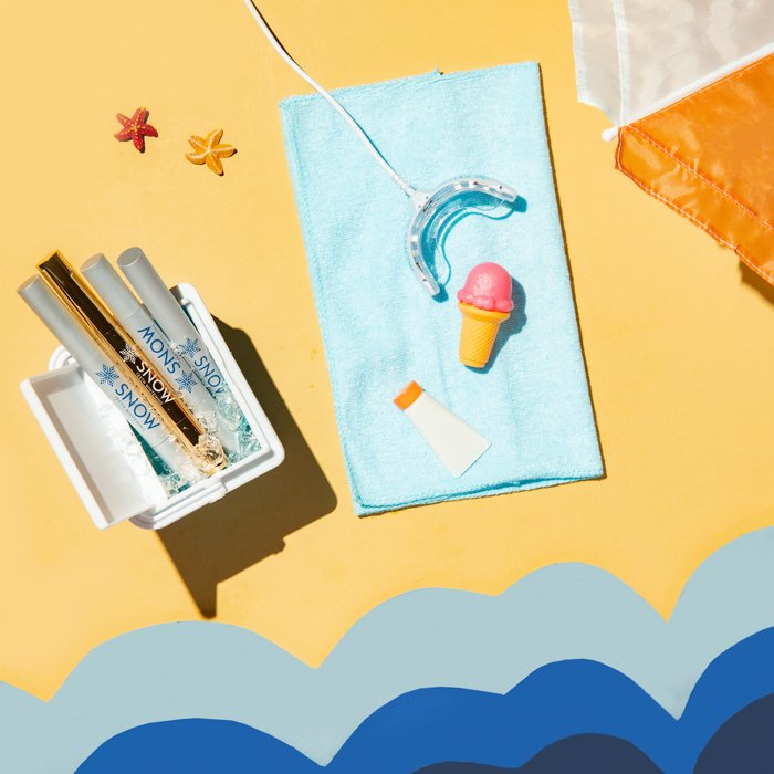 A flat lay product photography image of teeth whitening products in a miniature beach set