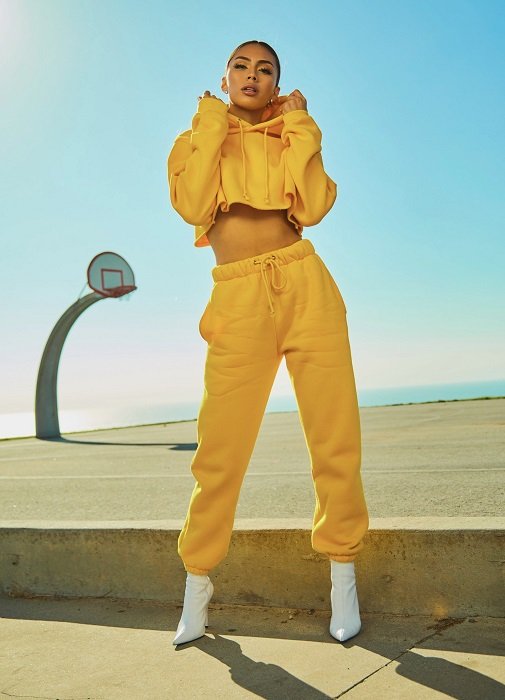 color block photoshoot ideas: a model in a yellow sweat suit poses in front of a basketball court and a bright blue sky