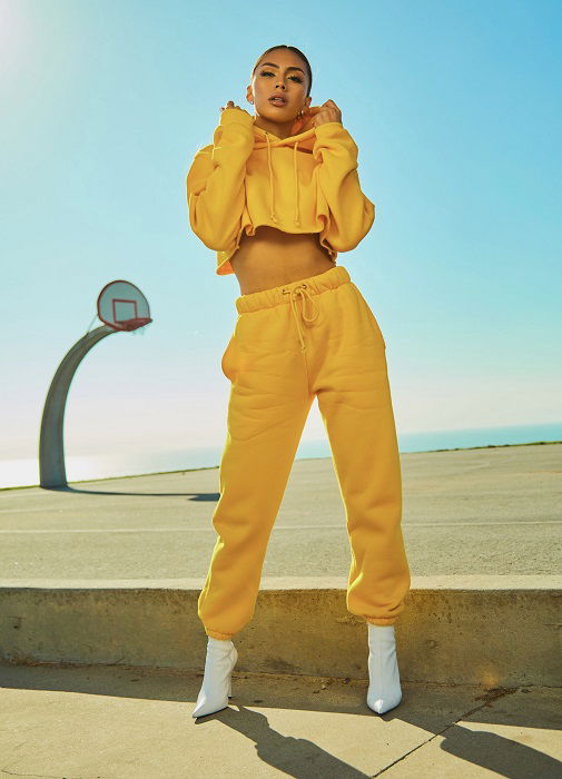 color block photoshoot ideas: a model in a yellow sweat suit poses in front of a basketball court and a bright blue sky