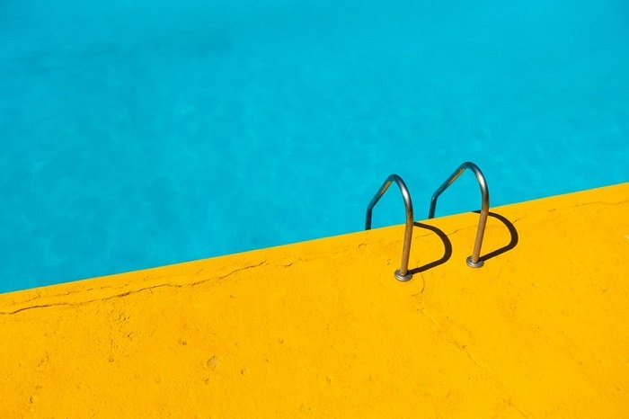 color blocking photoshoot tips: a minimalistic image of a pool ladder leading onto orange concrete
