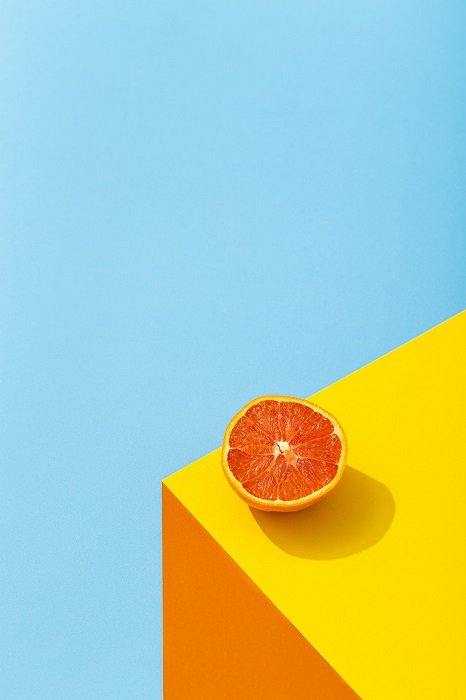 color block photoshoot ideas: minimalistic photo of an orange on a yellow and orange table with blue background