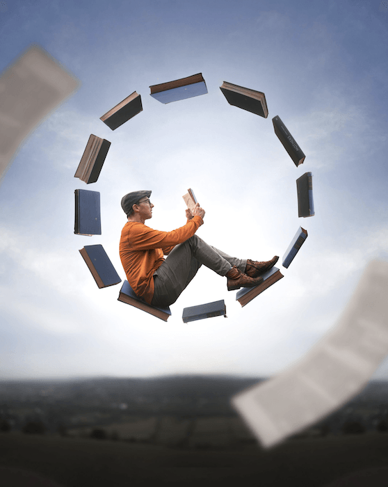 Composite photography image of a man sitting and reading on a circle of levitating books