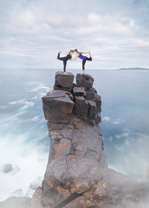 Composite photography image of women in a yoga pose on top of rock cliffs by water