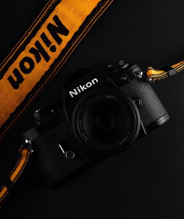 flat lay photograph of a black Nikon camera with a vibrant orange strap against a black background