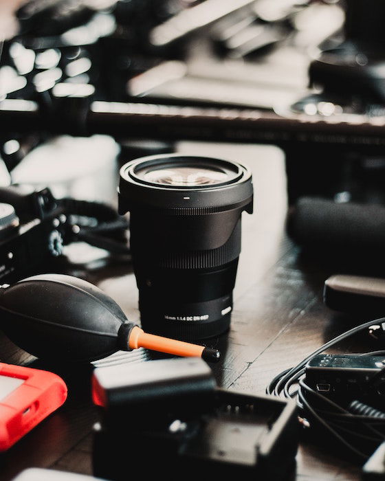 a Sony lens upright on a table surrounded by photo equipment