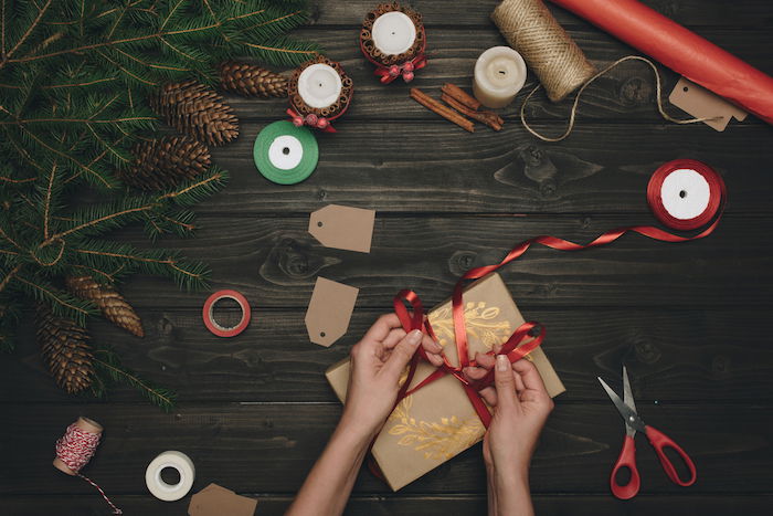 Christmas flay lay of person tying red ribbon on a wrapped present