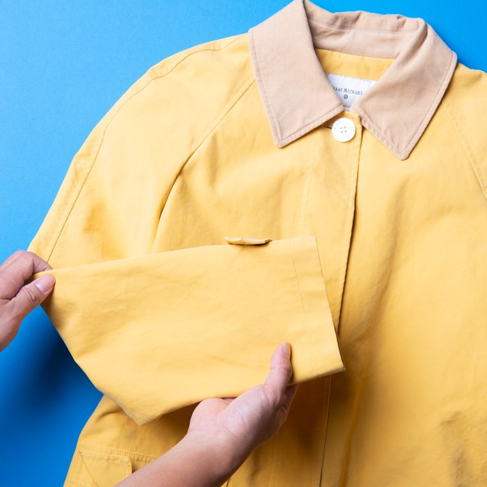 Flat Lay Photography of Clothing: Yellow coat being handled by a person for a clothing flat lay
