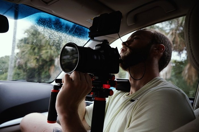 a videographer in the passenger seat of a car shooting the driver