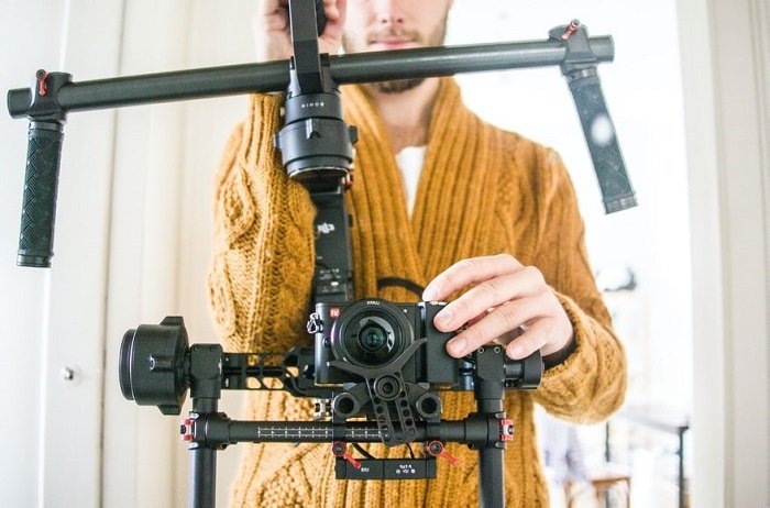 a head on shot of a videographer in a yellow sweater using a stabilizer on his DSLR